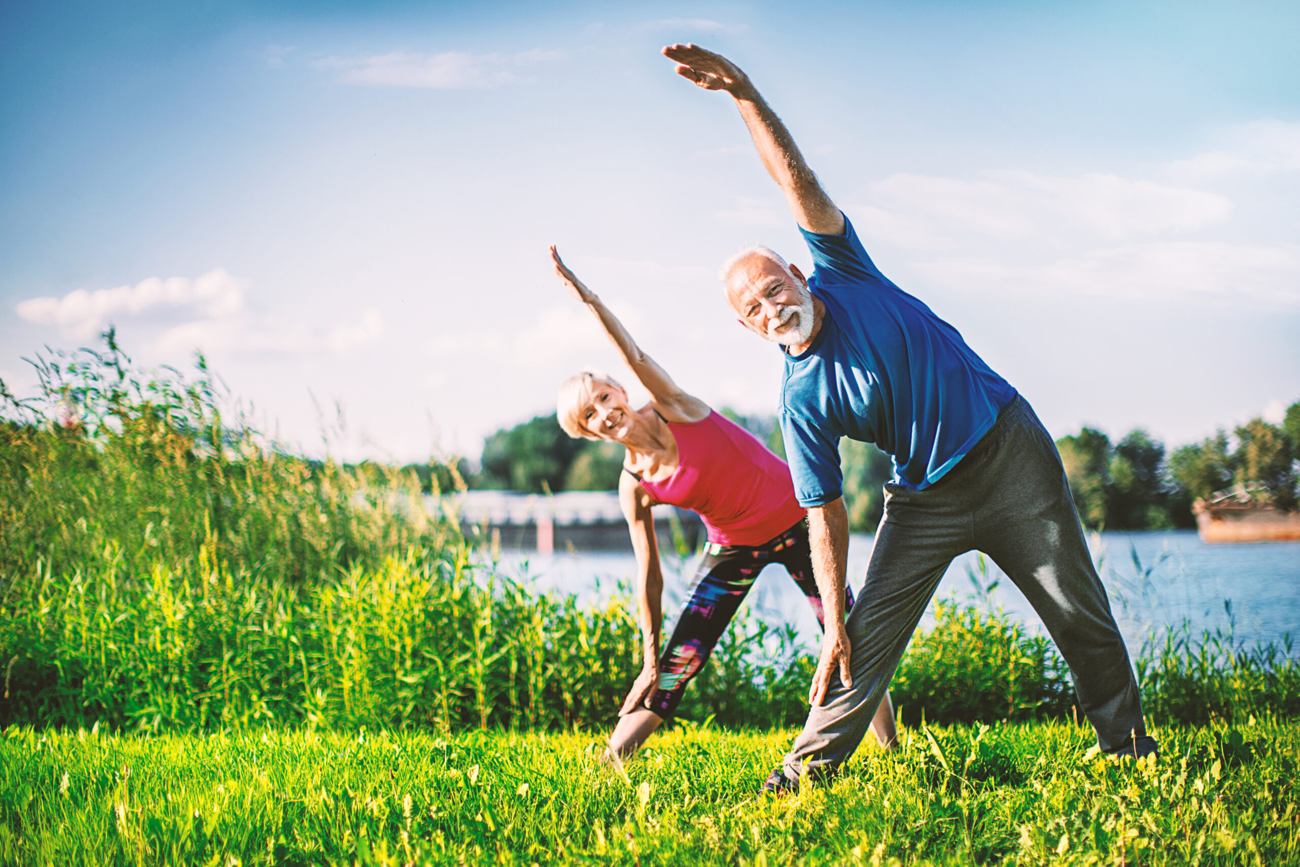Mature couple stretching and looking at camera outdoors. Front view. Horizontal.