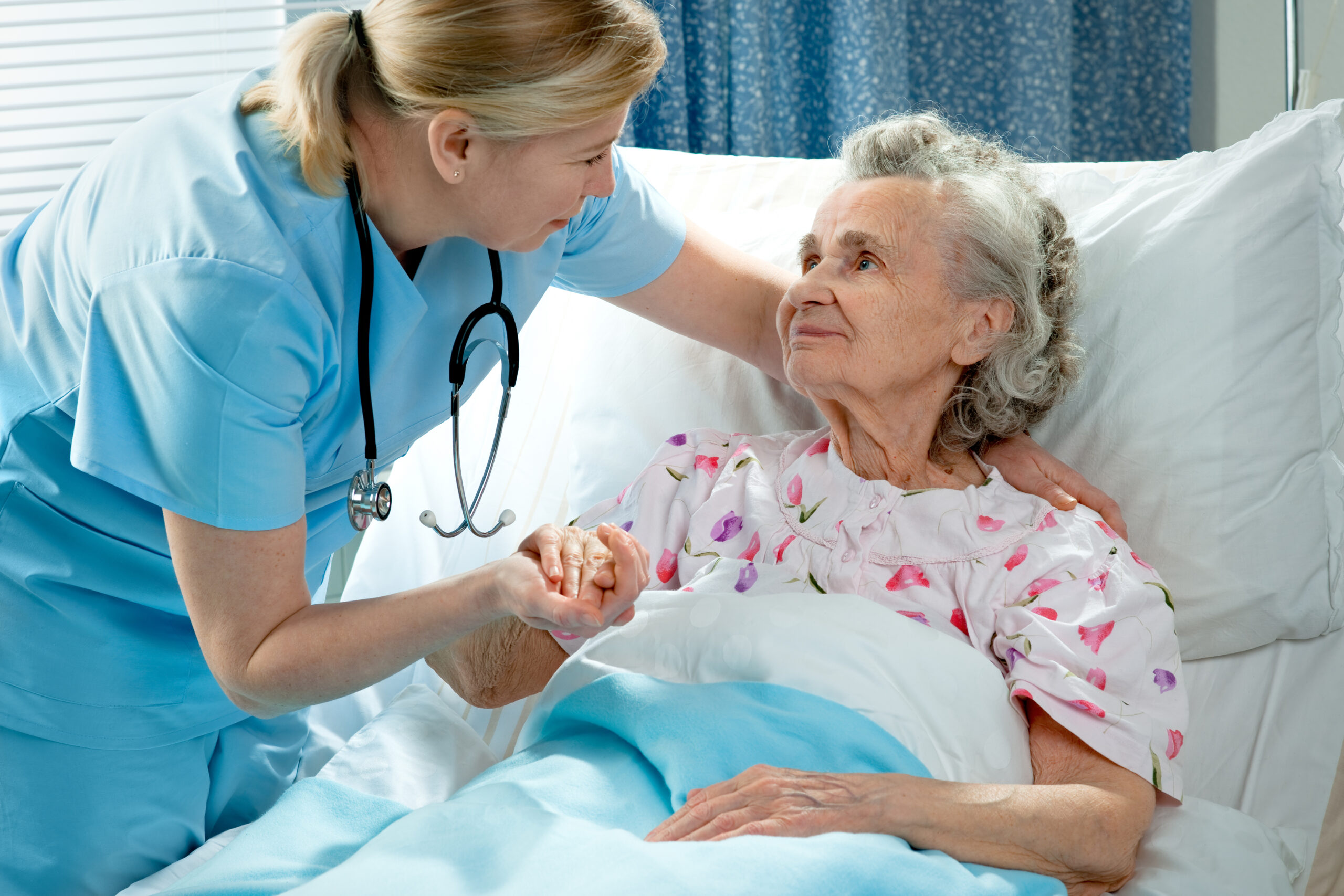 Nurse cares for a elderly patient lying in bed in hospital.
