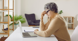elderly senior woman sitting at counter with laptop, confused and frustrated